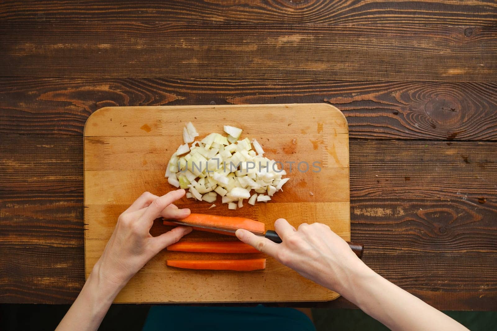 Unrecognizable woman cut carrot on a quarters with a knife, top view