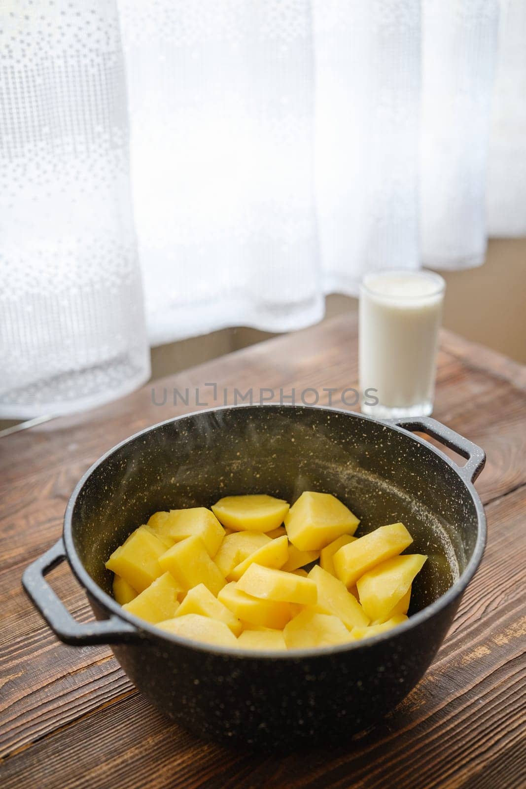 Kitchen table with boiled potatoes in a pot and glass of warm milk