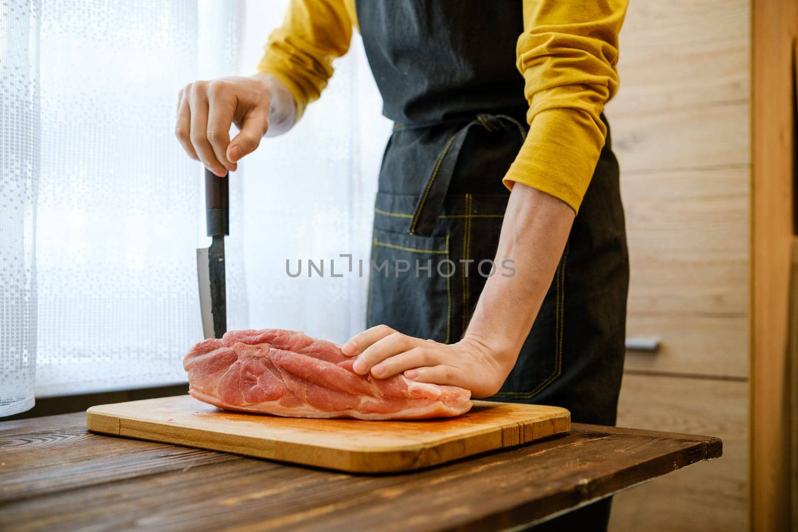 Unrecognizable man in the kitchen leans with one hand on a pork shoulder and with the other hand on a sharp knife