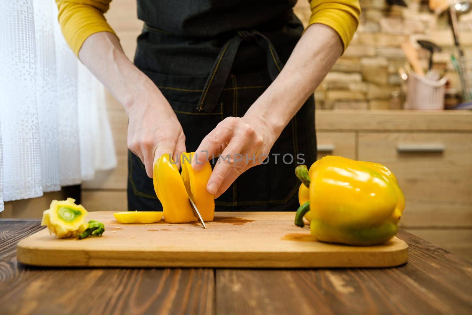 Unrecognizable man cutting on half bell peppers on wooden cutting board