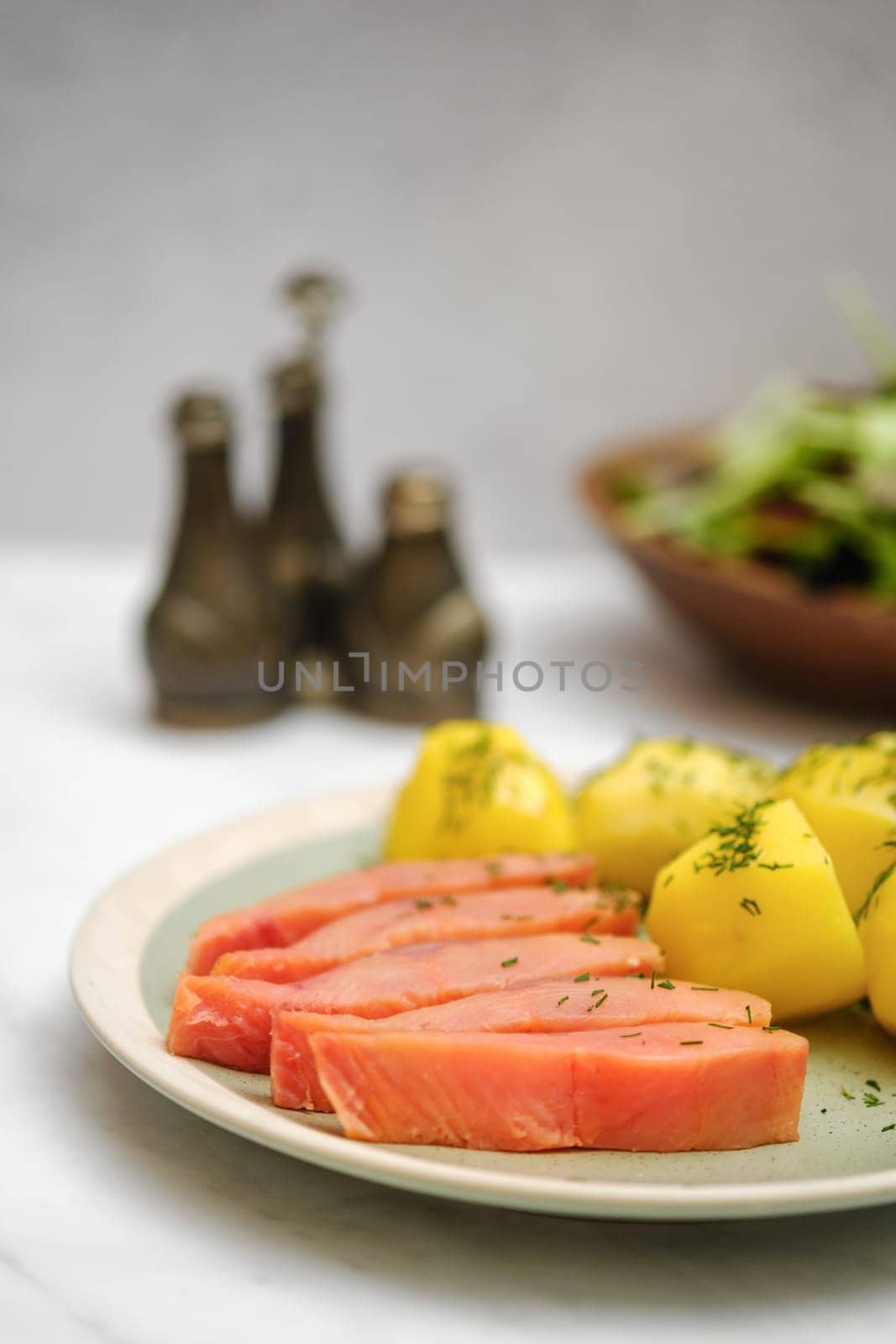 Closeup view of plate with hot smoked humpback salmon and boiled potatoes with fresh green salad on a marble table