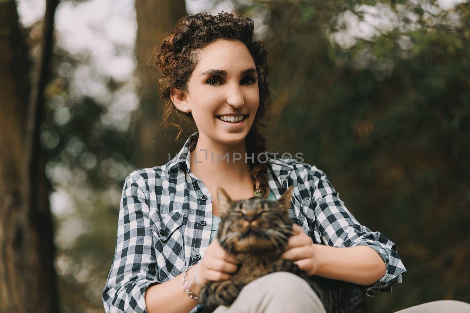young woman with curly hair and a checkered shirt holds a very content tabby cat. Both appear happy, with the cat looking like it's enjoying a spa experience