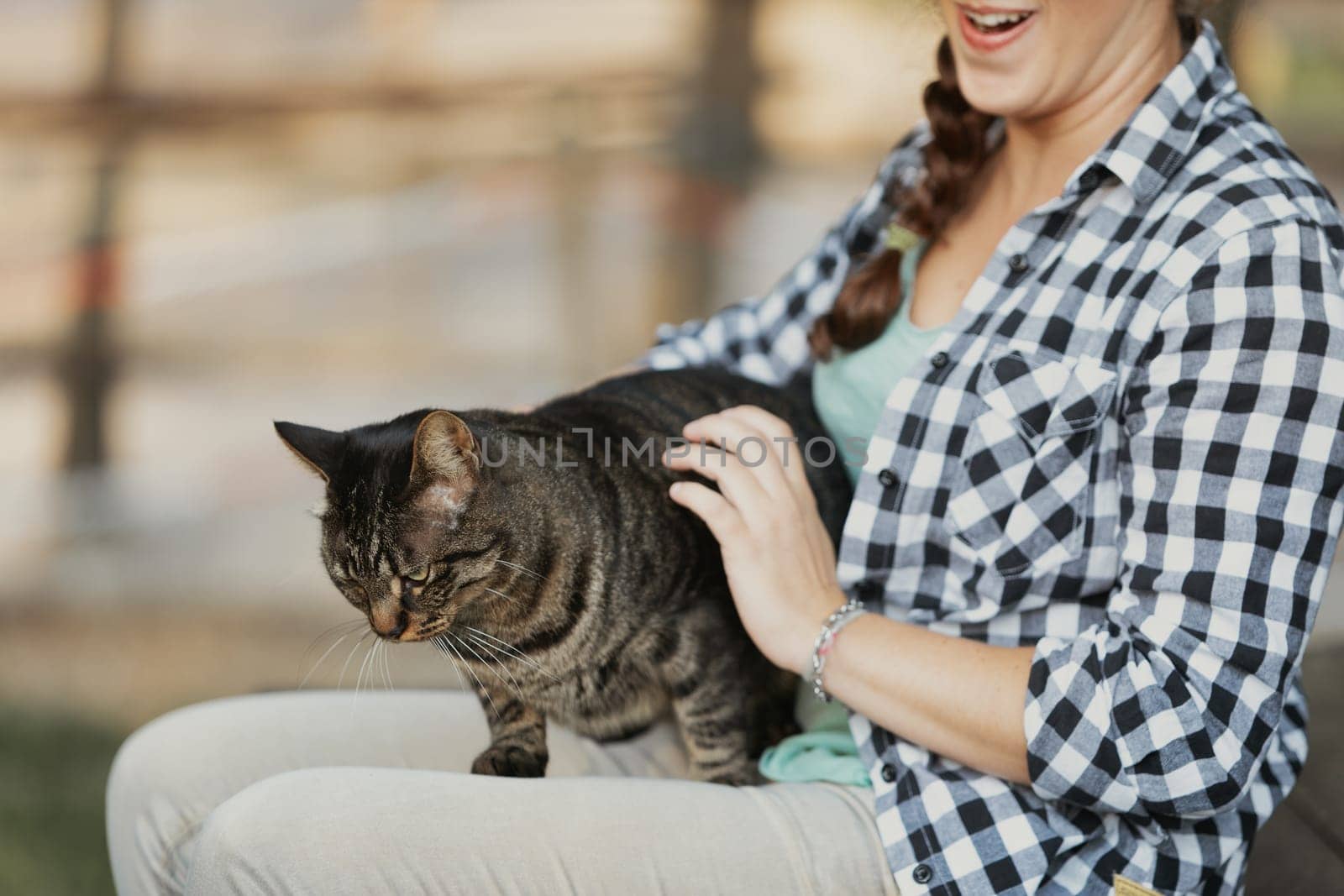 woman in a checkered shirt with curly hair holds a blissful tabby cat. The cat’s serene expression suggests it is enjoying a luxurious spa experience
