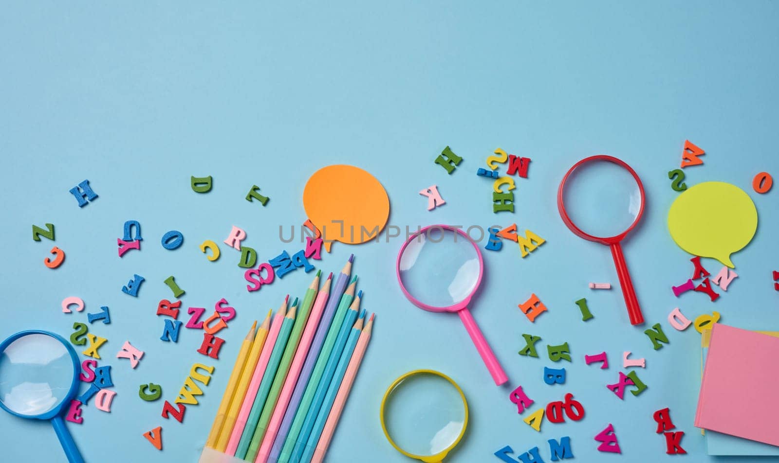 Stationery laid out on a blue background. Multi-colored  sticky notes and wooden letters, preparing for study or work, organizing workspace