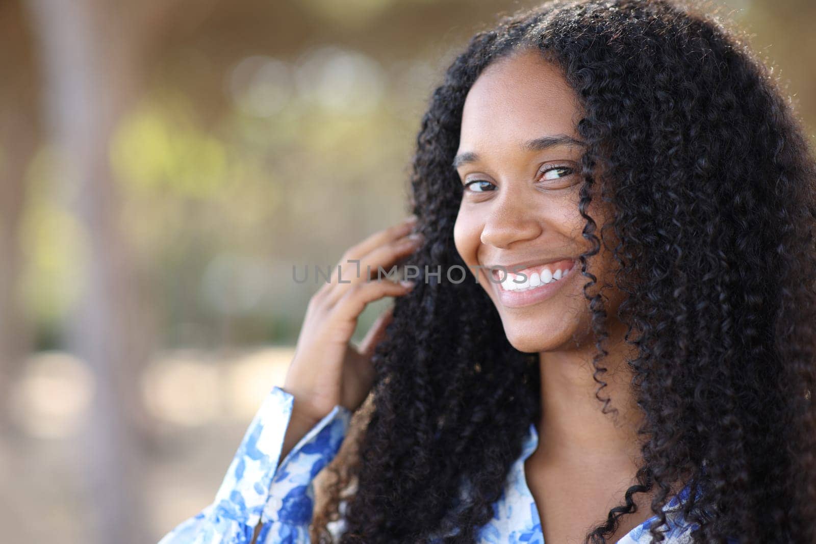 Black woman with white smile looking at you in a park