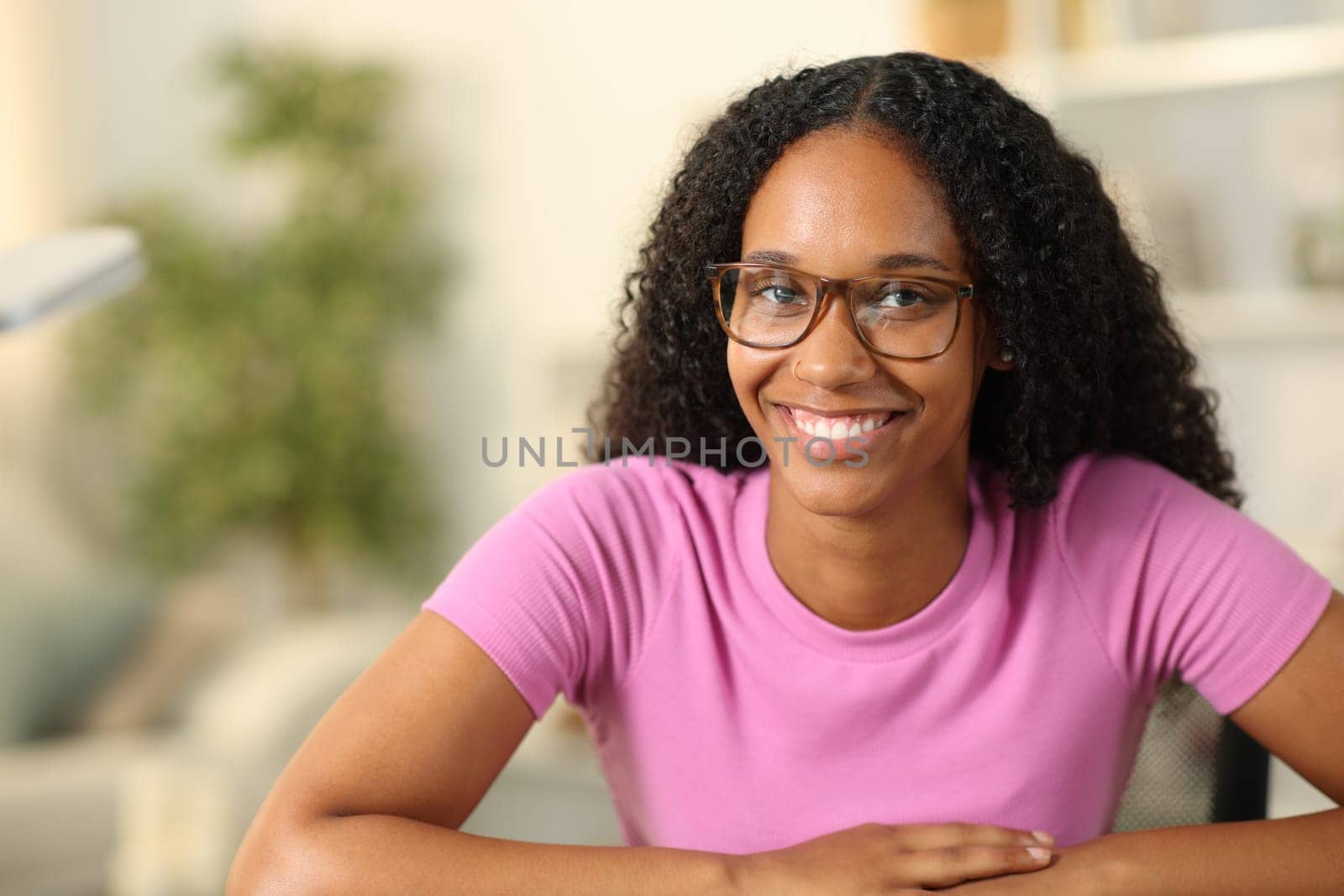 Happy black woman with eyeglasses looks at you at home