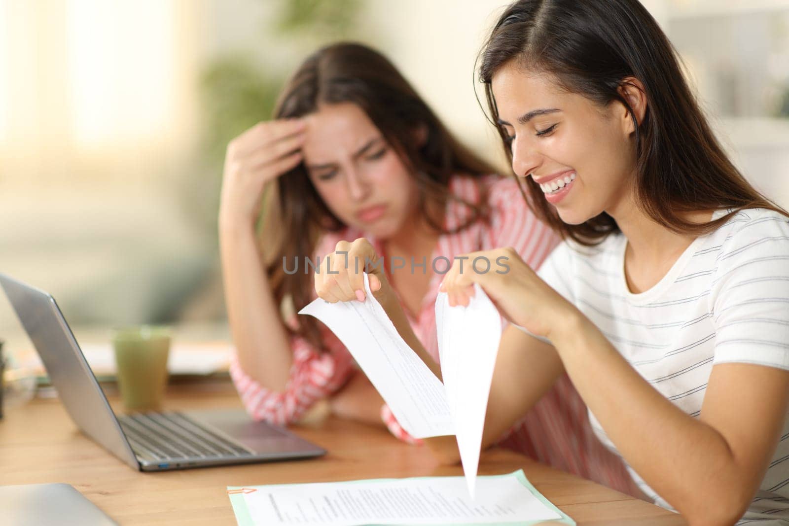 Happy woman breaking contract beside a sad colleague at home