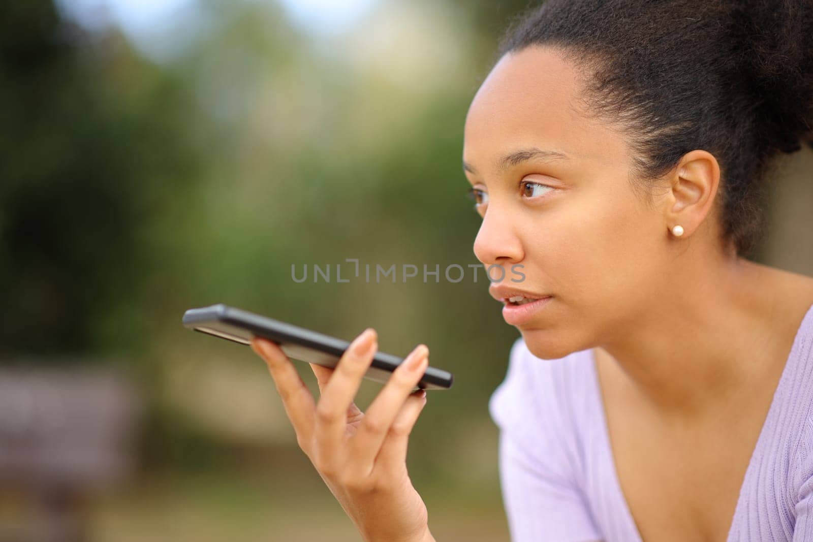 Serious black woman dictating message on phone in a park
