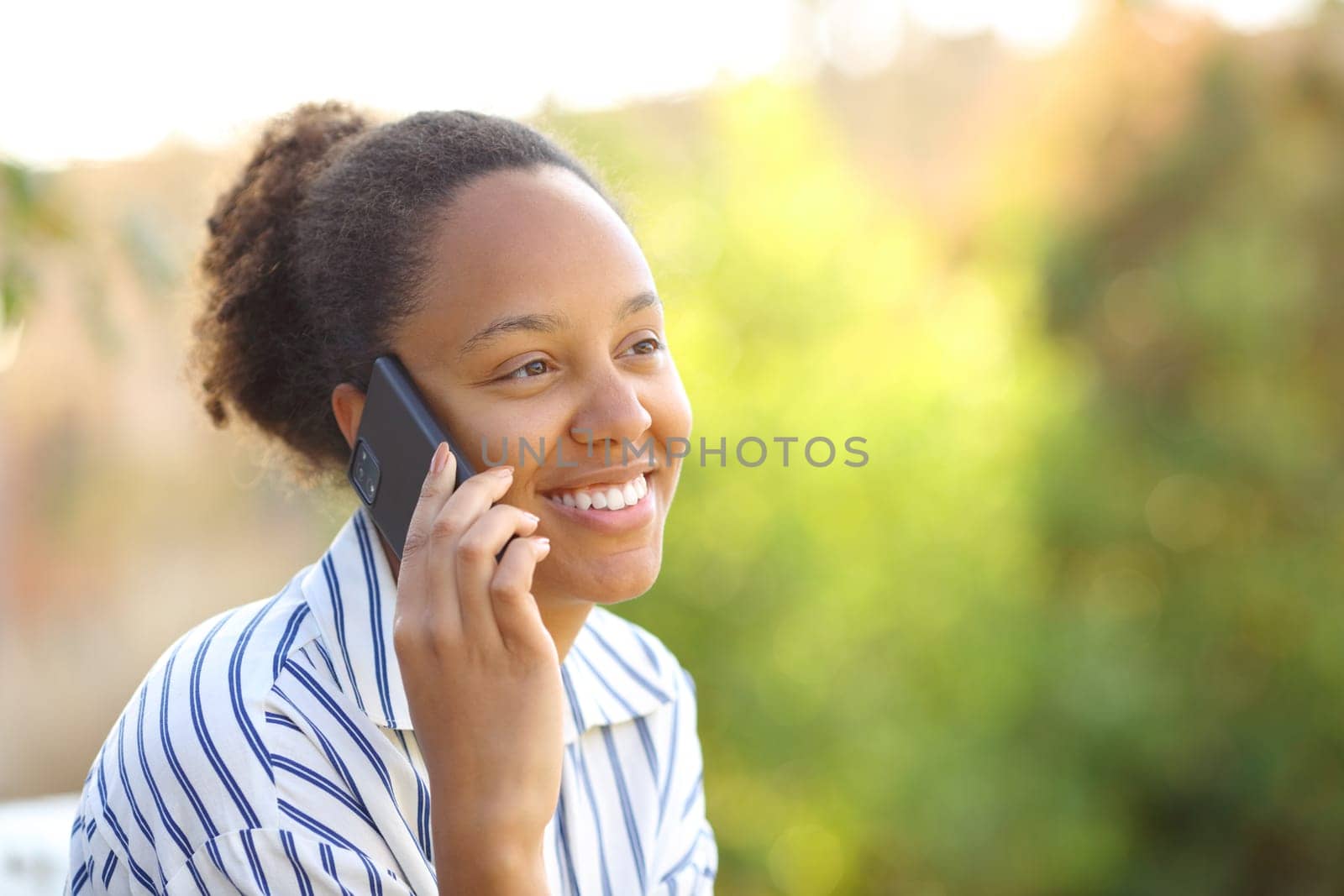 Happy black woman talking on phone sitting in a park