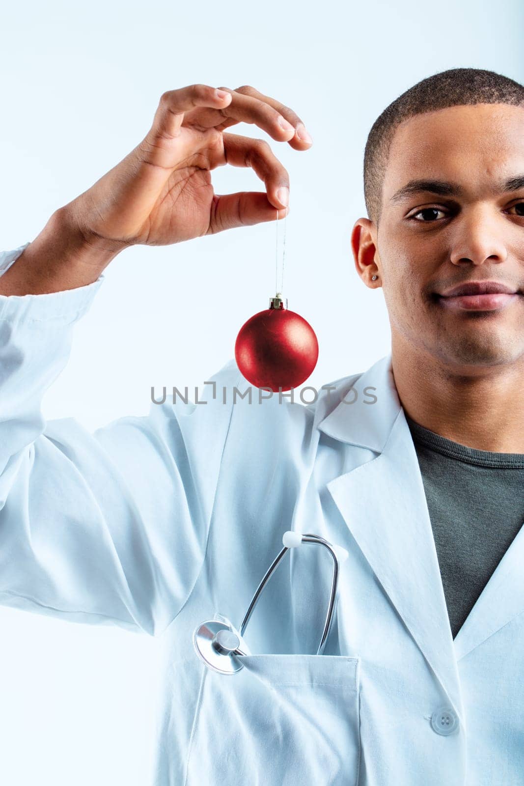 Individual in a white lab coat, holding a red ornament and smiling gently. This military doctor is dedicated to improving his patients' health during the Christmas season