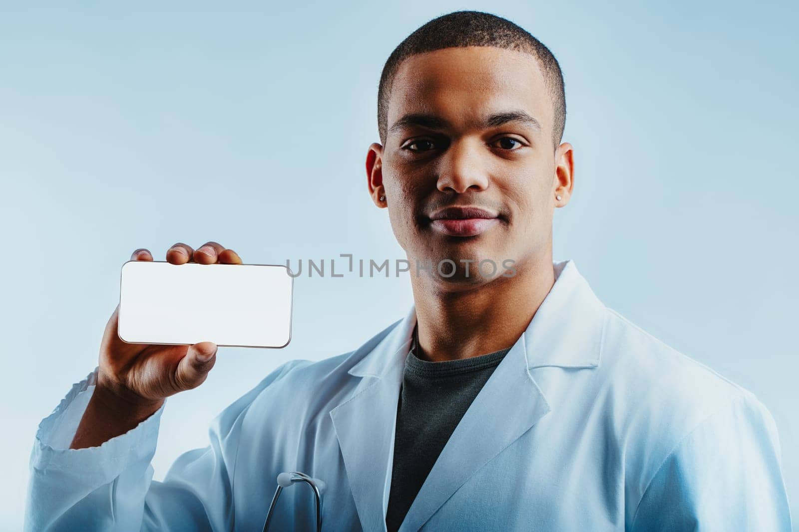 Man in a white lab coat, holding a smartphone and smiling confidently. As a military doctor, he promotes the use of medical mobile apps for better healthcare solutions