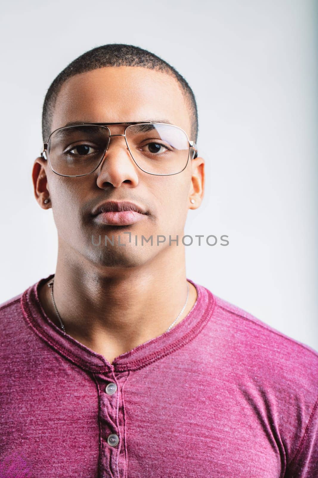 Young man with a serious expression, wearing aviator glasses and a maroon henley shirt. His focused look and casual attire suggest confidence and a relaxed, yet attentive attitude