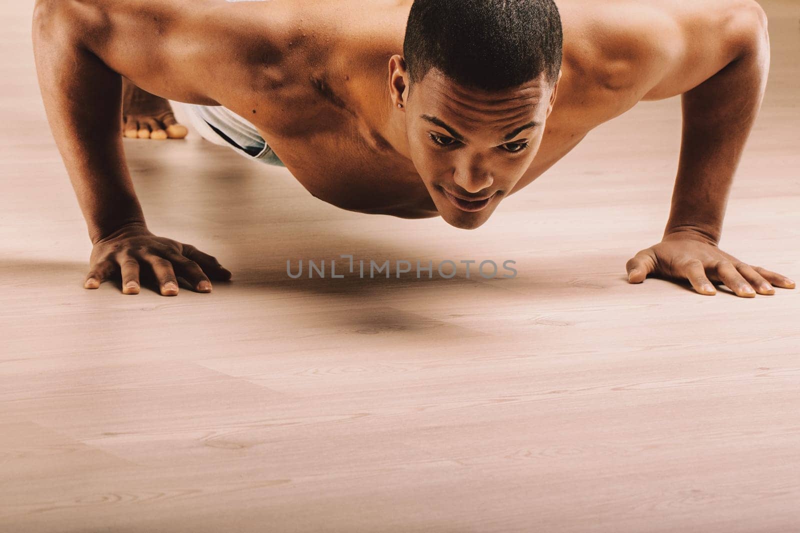 Focused young man performing push-ups, displaying a strong and muscular build. His intense expression and short hair reflect determination and physical fitness, highlighting his commitment to exercise