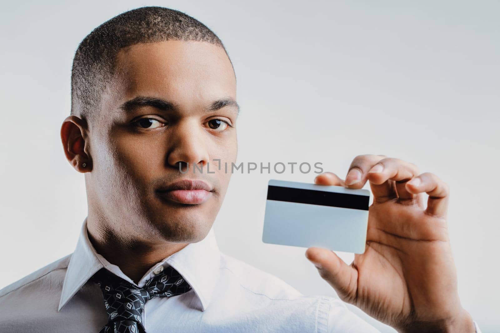Young professional in a white shirt and patterned tie, offering a business card. His confident expression and formal attire convey a sense of readiness for professional interactions