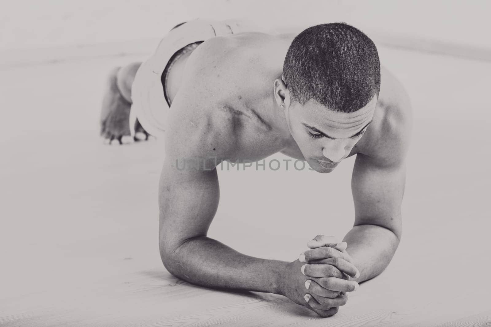 Muscular man performing a plank exercise on a wooden floor, old-skool strength and endurance. His focused expression and clenched hands emphasize determination and physical effort