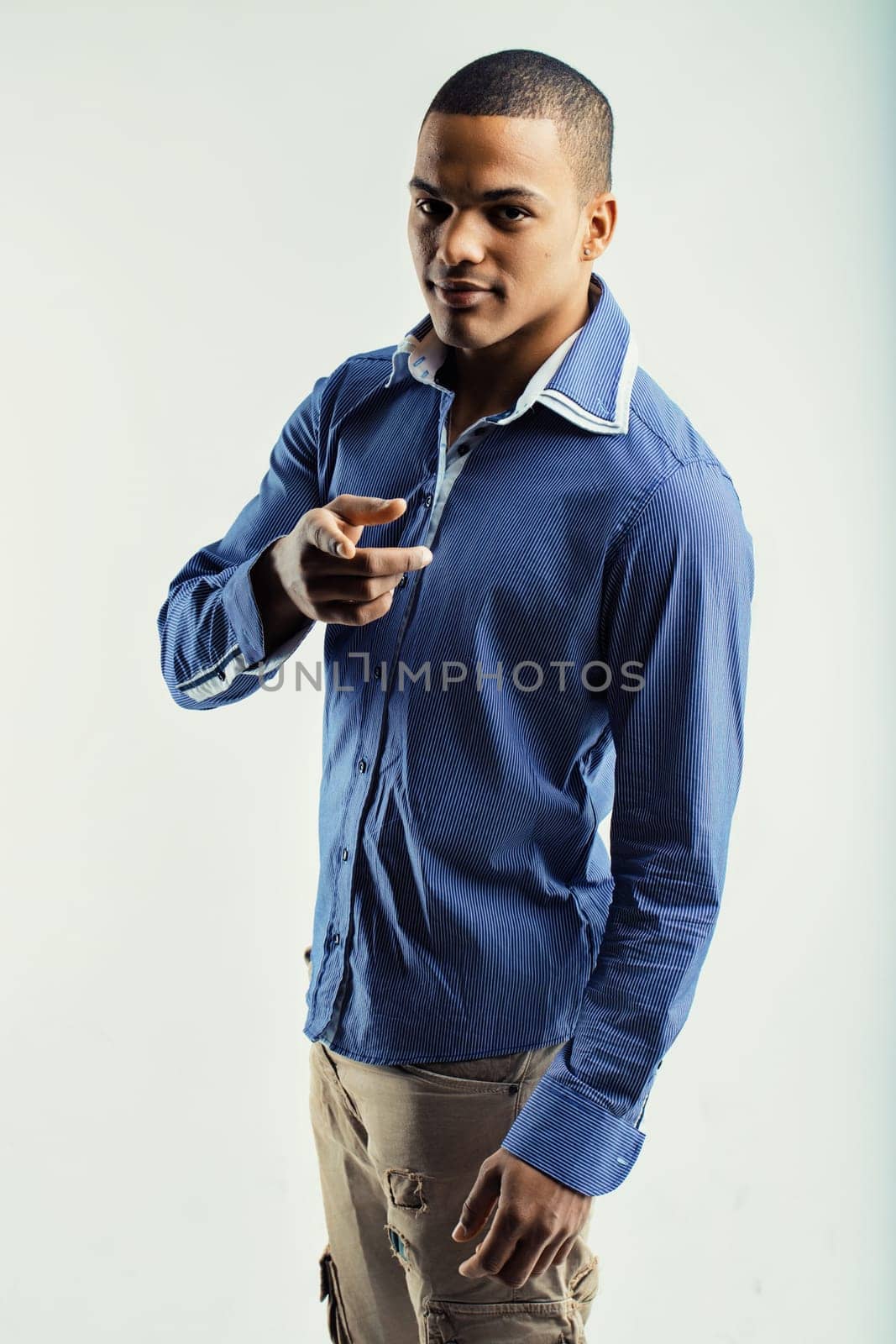 oung man in a blue striped shirt and beige pants, pointing forward with a confident expression. His casual attire and assertive gesture convey confidence and directness