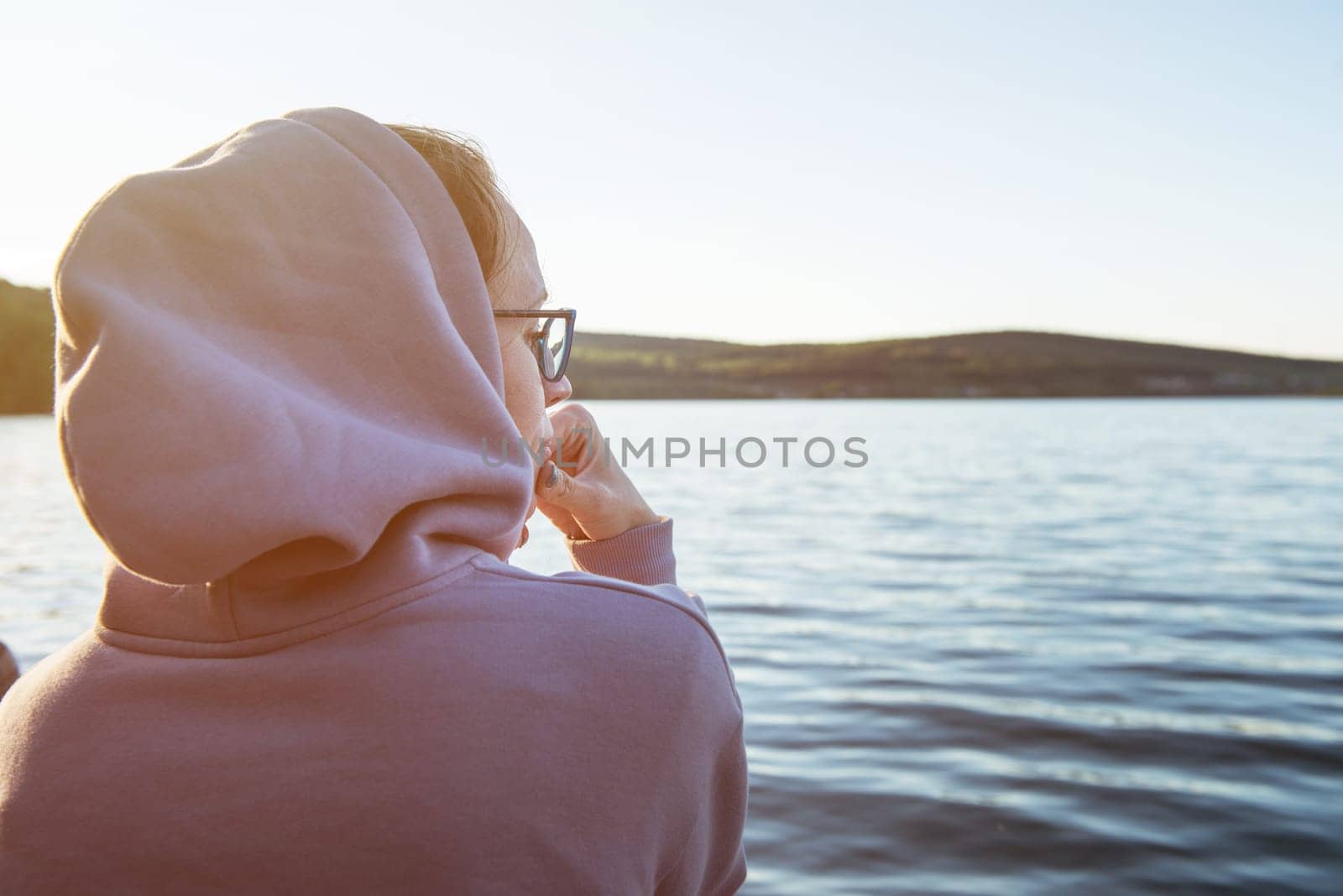 Young beautiful woman sitting on the pier with copy space, summer sunset