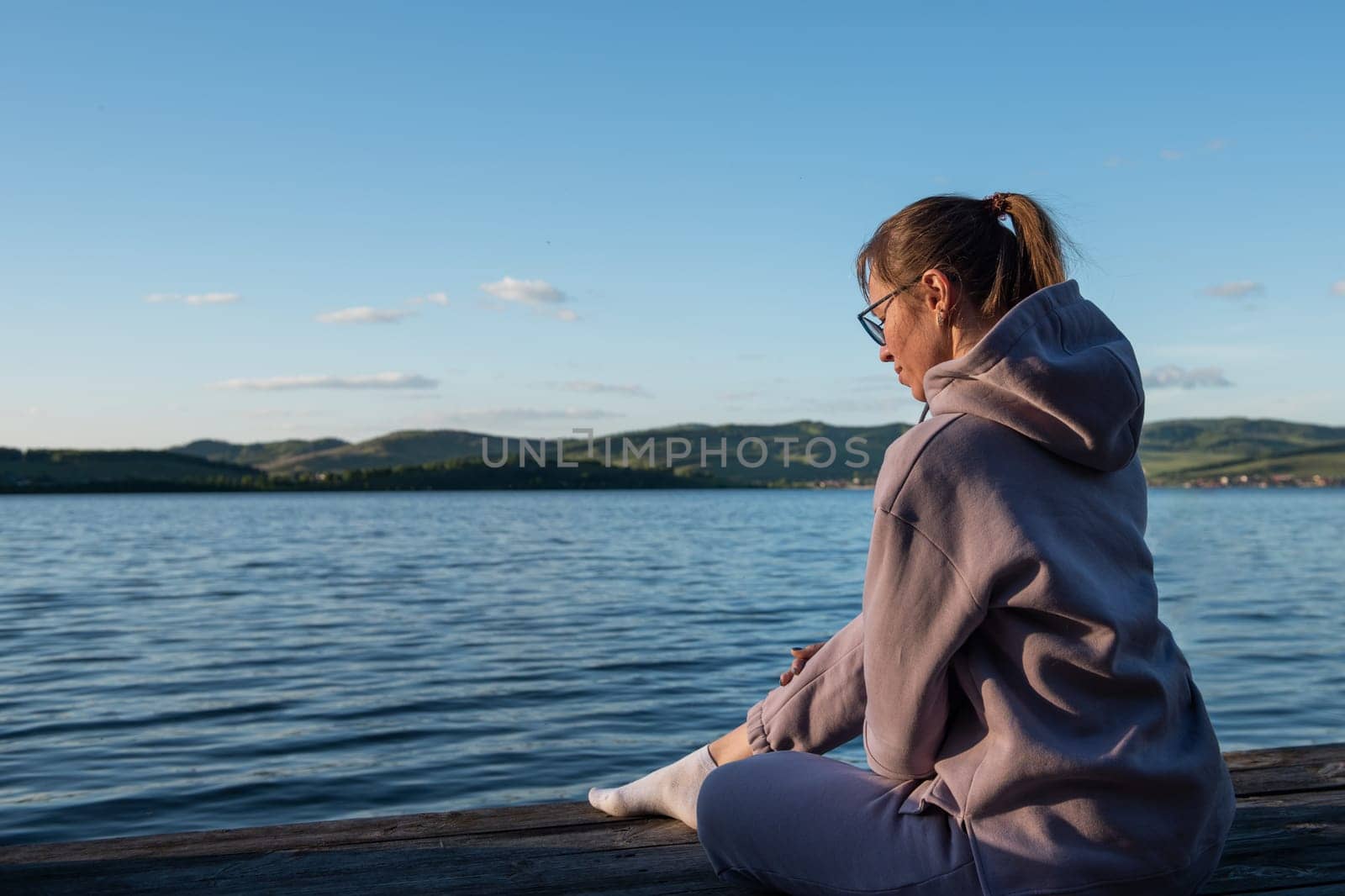 Young beautiful woman sitting on the pier with copy space, summer sunset