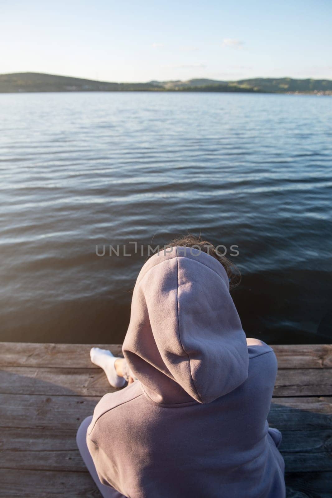 Young beautiful woman sitting on the pier with copy space, summer sunset