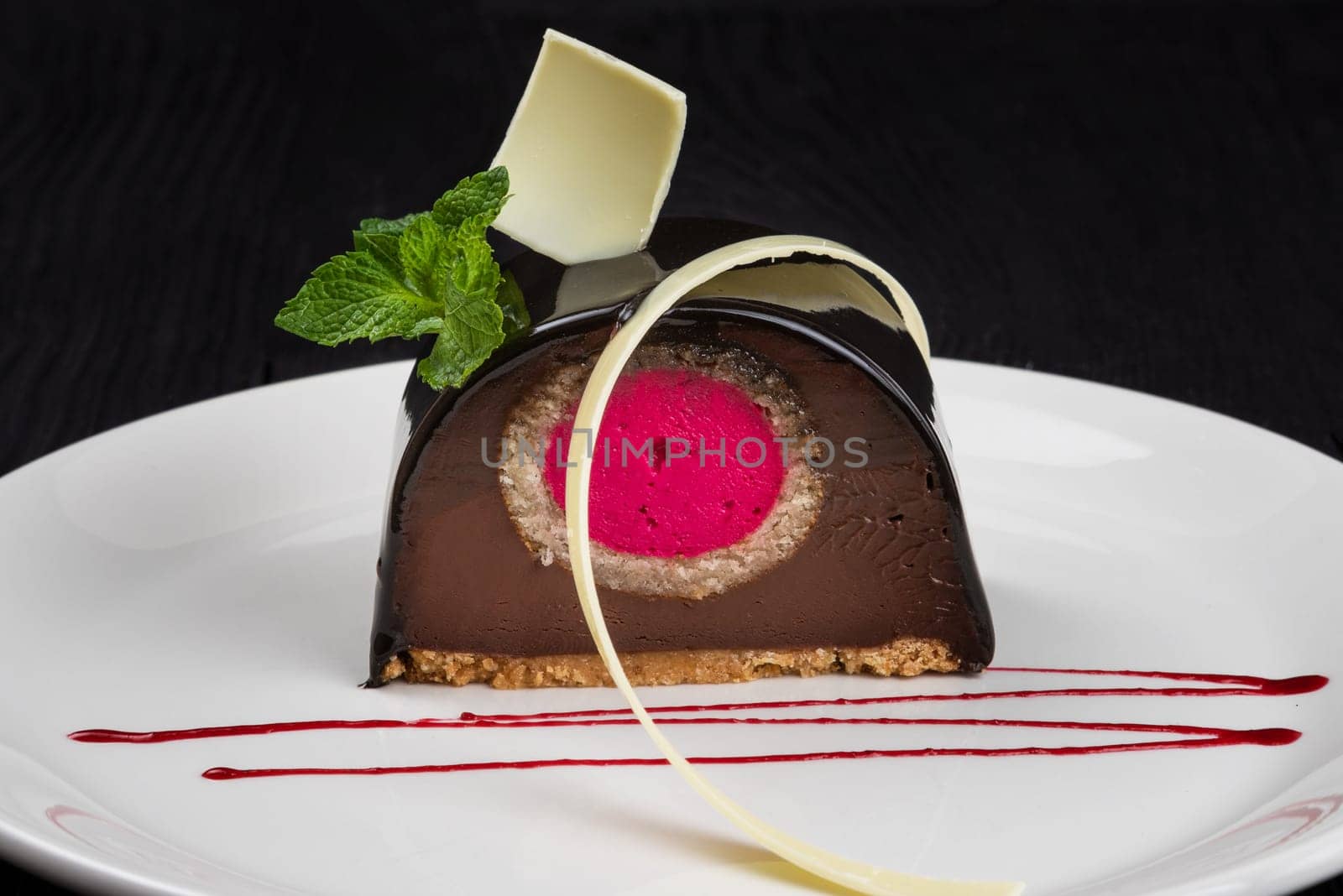 Delicious biscuit chocolate cake closeup with pink souffle decorated with mint and white chocolate on dark background