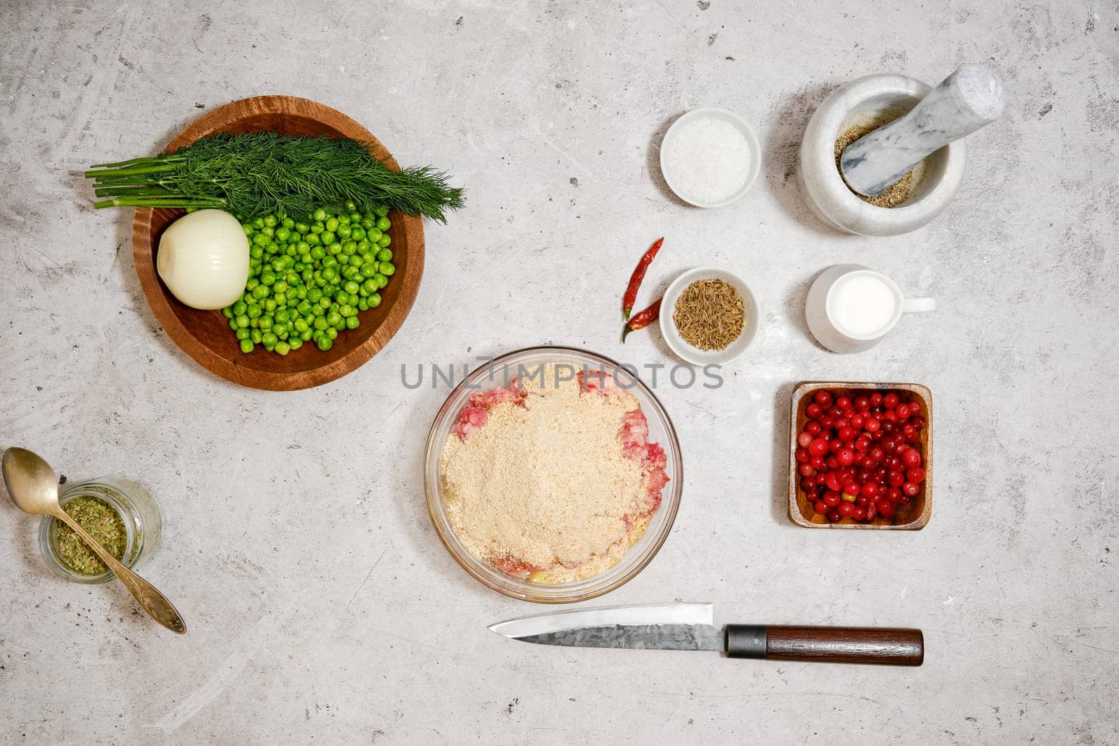 Top view of bowl with minced meat, egg and breadcrumbs surrounded with cranberry and green peas for sauce