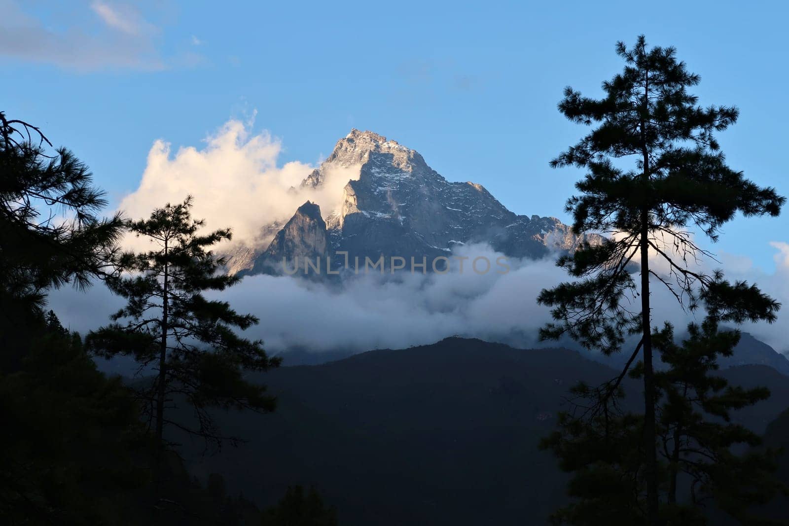 The peak of Mount Khumbila at sunset, view between the trees from the monastery of Monjo, Manjo village, Mount Everest Basecamp Trek, EBC, Nepal 2022