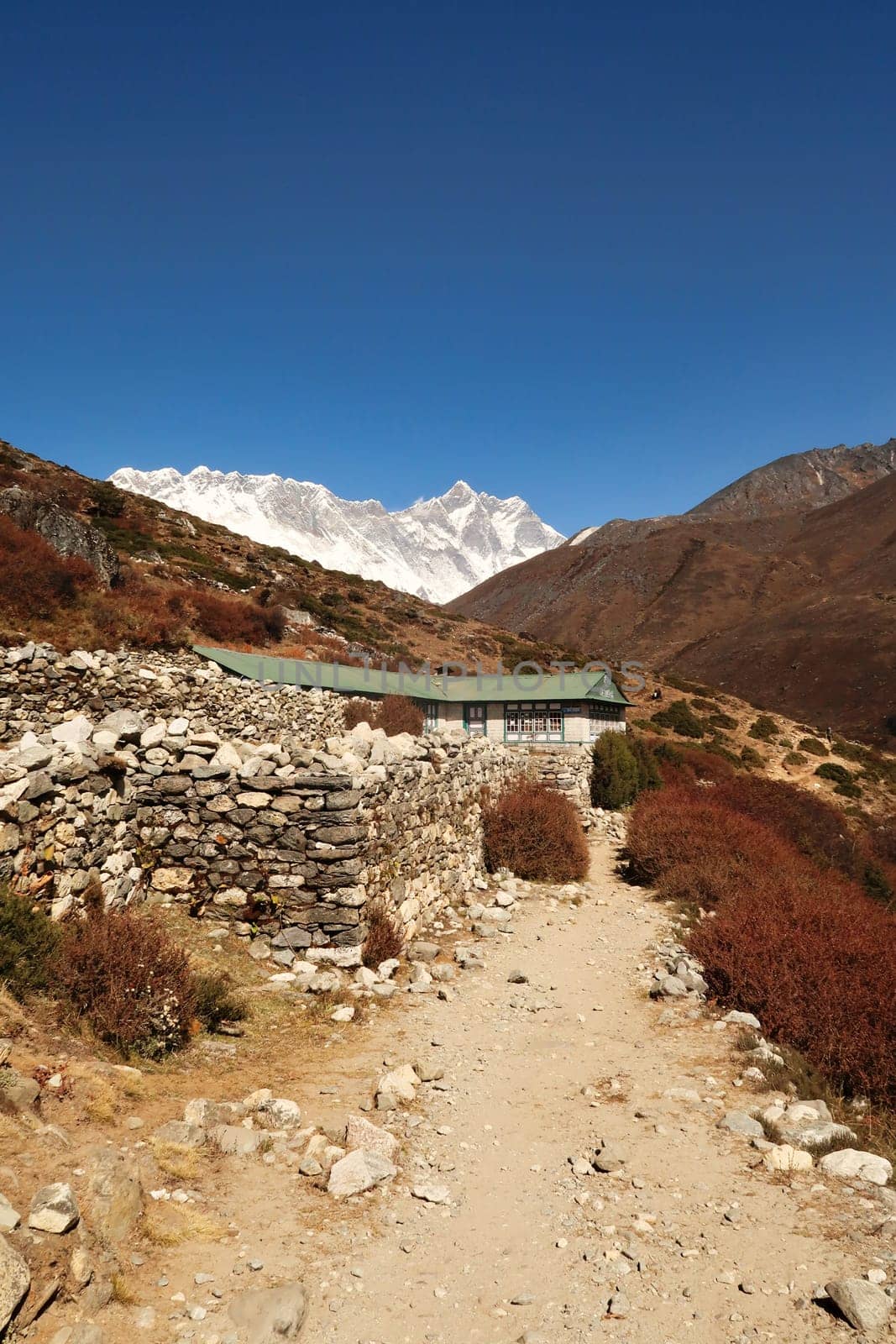 A teahouse surrounded by a stone wall outside of the village of Shomare, Mount Nuptse and Lhotse can be seen in the background, Mount Everst Base Camp Trek, EBC, Nepal 2022