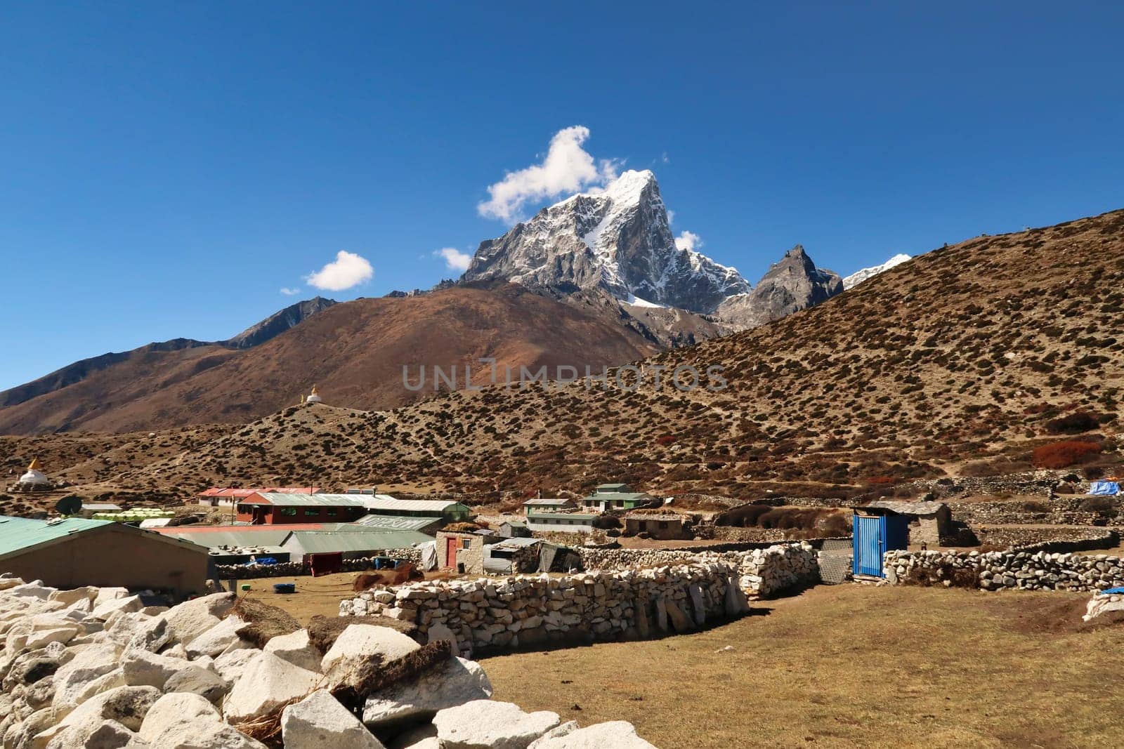 Walking through dingboche village, houses with stone walls in the foreground, two pagodas in front of the peak of Mount Tobuche in the background, Mount Everest Base Camp Trek, EBC, Nepal 2022