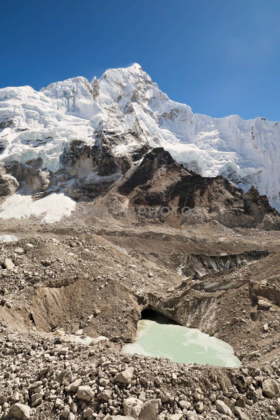 View up to the snow covered peak of Mount Nuptse, from the Khumbu Glacier with a little pond, hole filled with green melt water in the foreground, Mount Everest Base Camp Trek, EBC, Nepal 2022