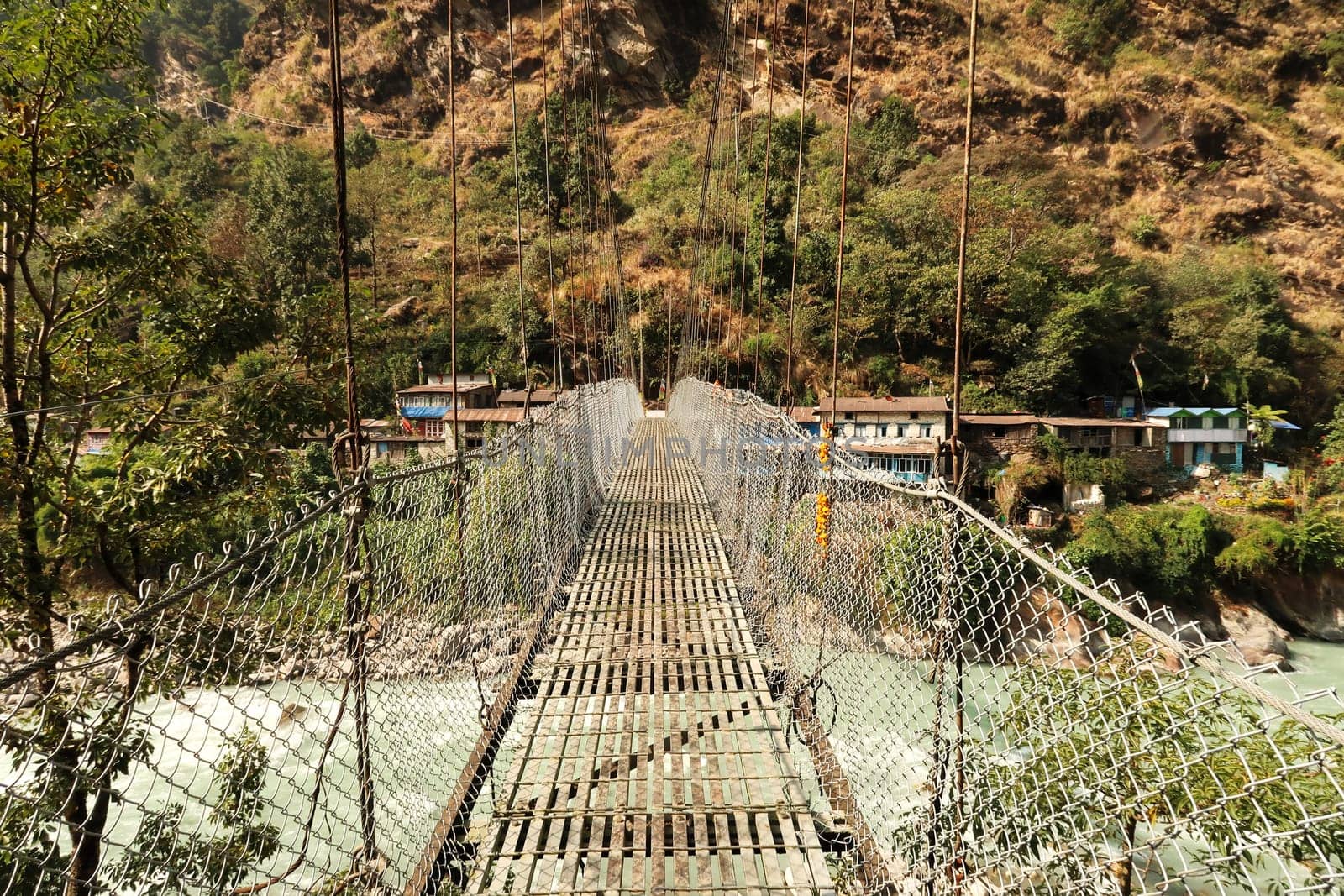 Crossing the metal suspension bridge over the Marsyangdi River leading into Syanche village, Annapurna Circuit Trek, Nepal 2022