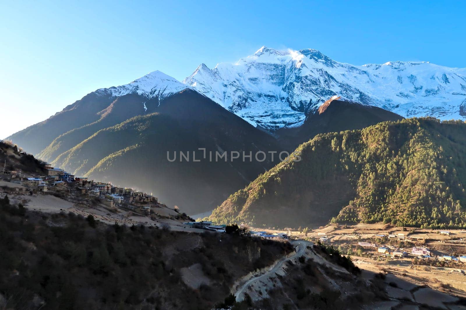 View onto the villages of Upper Pisang and Lower Pisang in front of Annapurna II, IV in the early morning, Upper Pisang is still in the shade while Lower Pisang is in the sun, Annapurna Circuit Trek, Nepal 2022