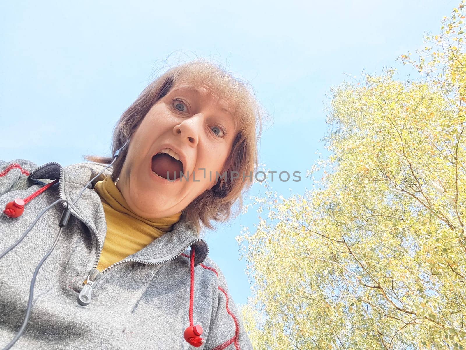 Woman captures a joyful moment while exploring a vibrant autumn landscape filled with golden leaves and clear skies.