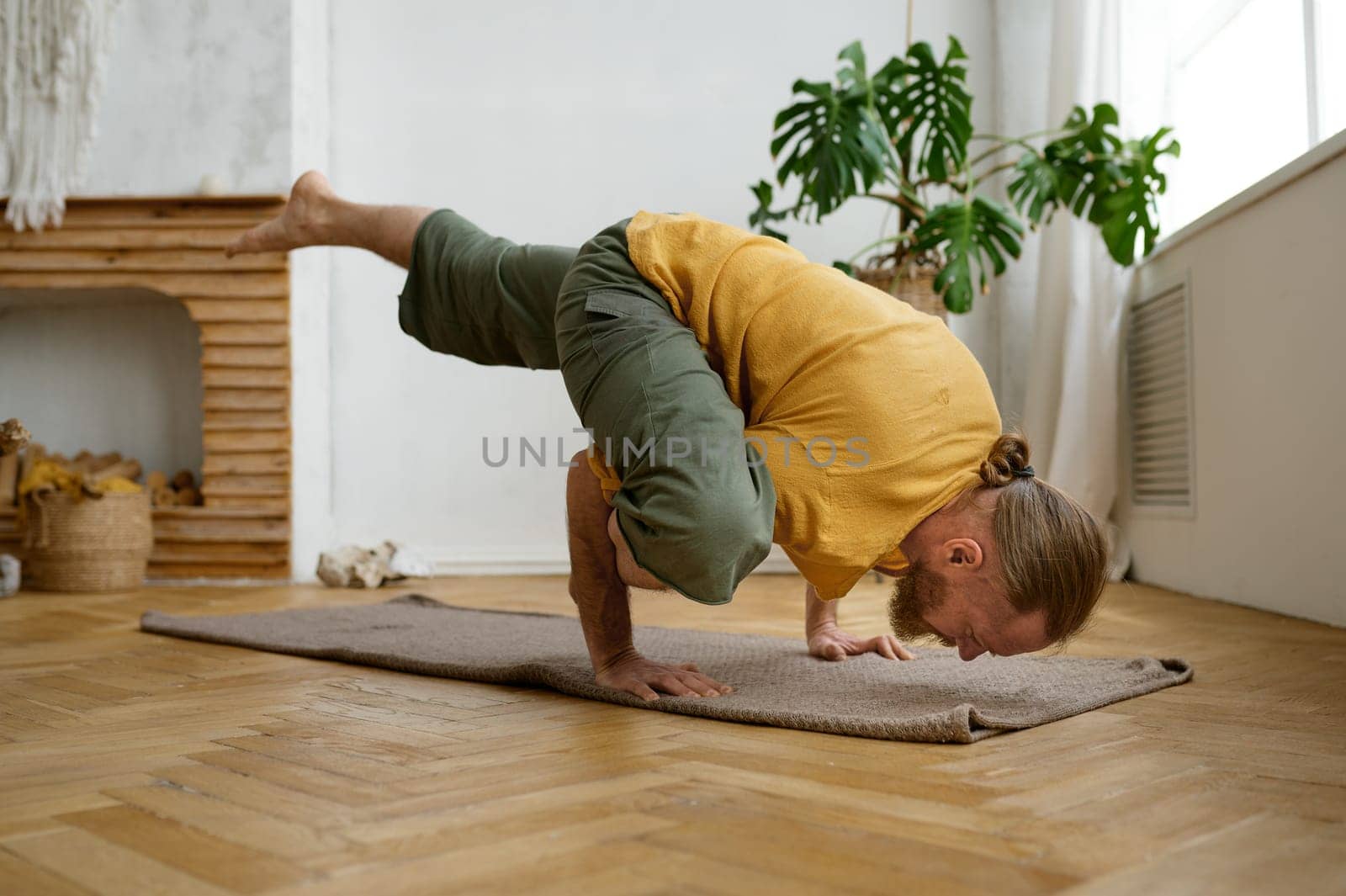 Sporty muscular man practicing hand standing yoga pose at home living room. High level fitness exercises