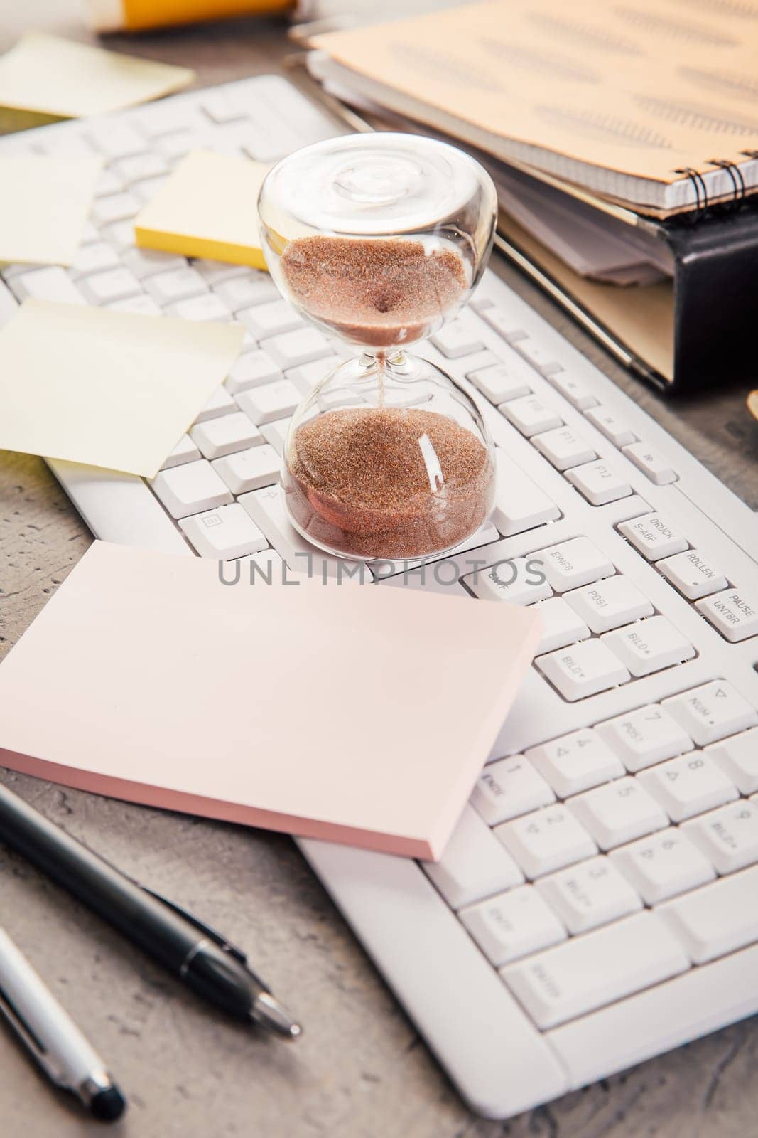 Crop of hourglass on home office table count measure time.  Workplace of busy employee, time management and burnout concept