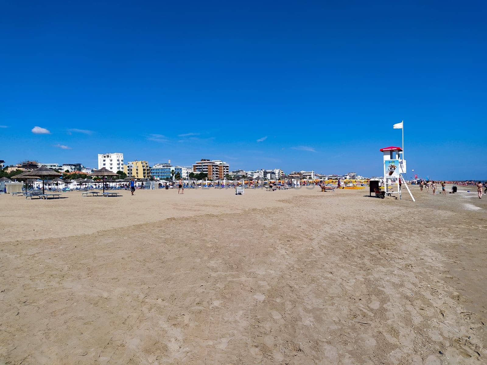 Rimini, Italy - June 25, 2024: People going along Rimini beach. The sunbeds and parasols on the beach