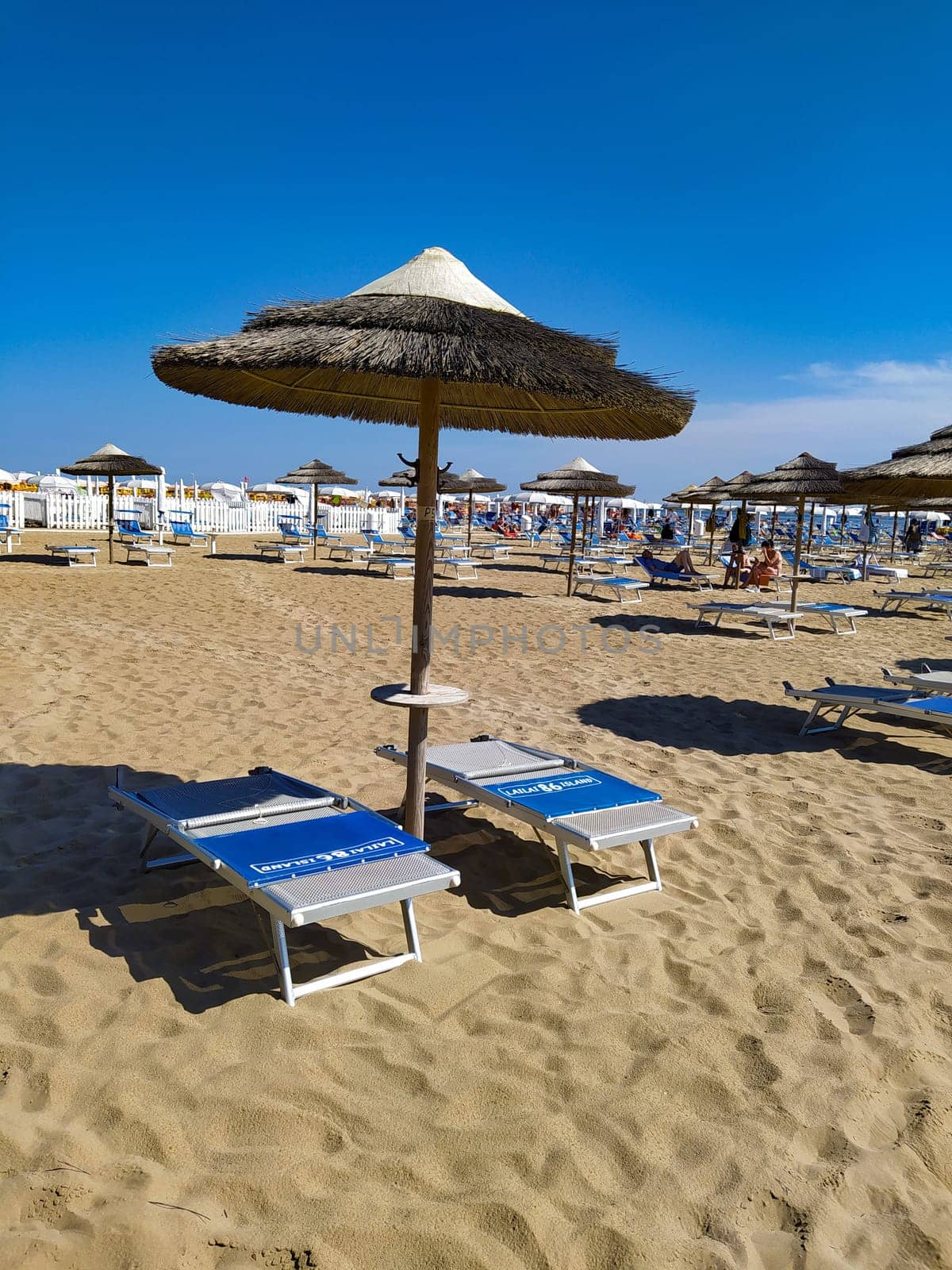 Rimini, Italy - June 25, 2024: People going along Rimini beach. The sunbeds and parasols on the beach