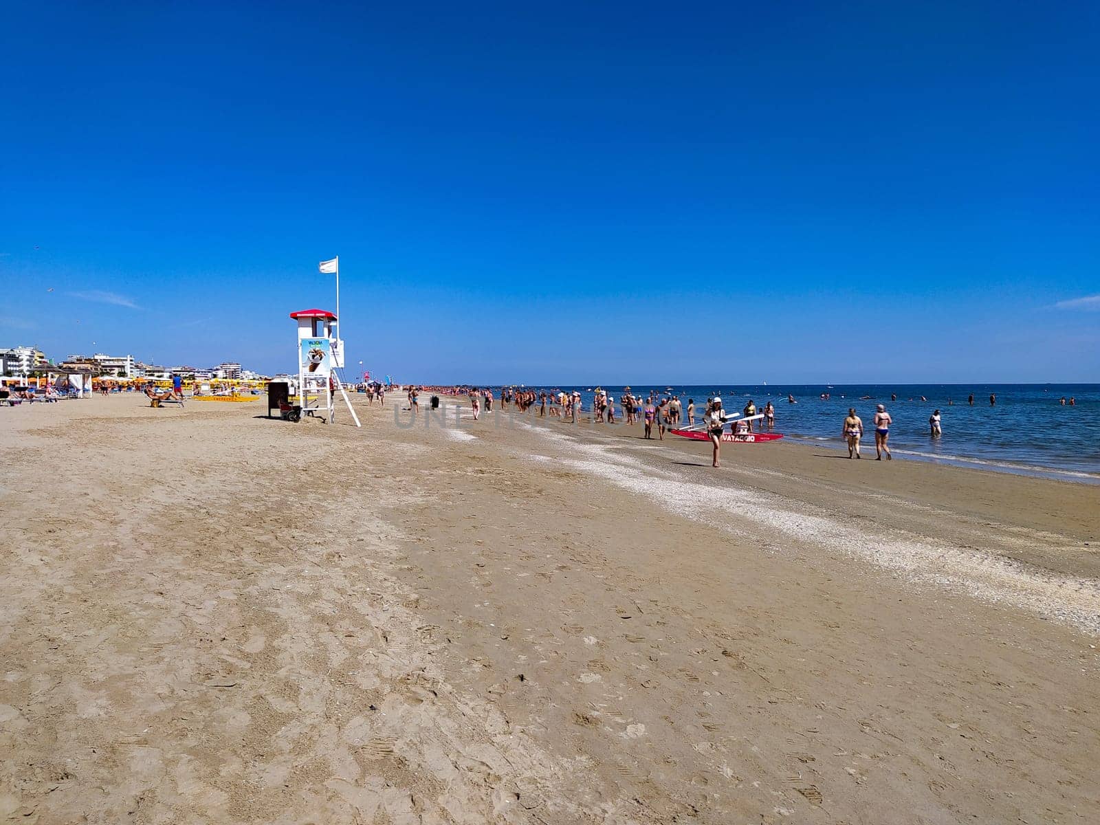 Rimini, Italy - June 25, 2024: People going along Rimini beach. The sunbeds and parasols on the beach