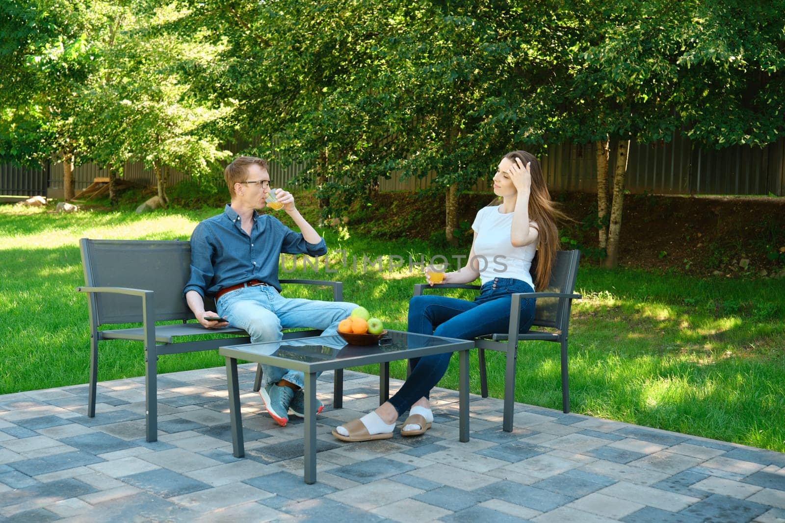 Father and daughter are sitting at a patio table with refreshing drinks on a sunny day in the backyard