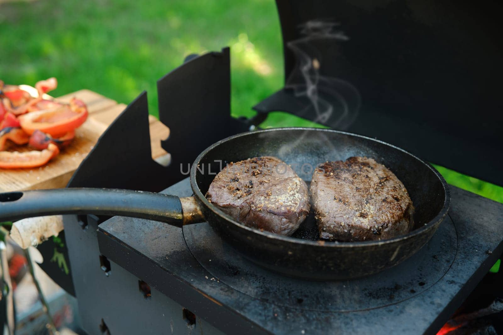 Two pieces of beef steak in a frying pan on outdoor grill