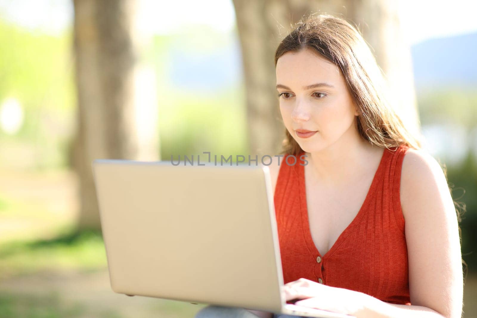 Serious woman in red using laptop sitting in a park