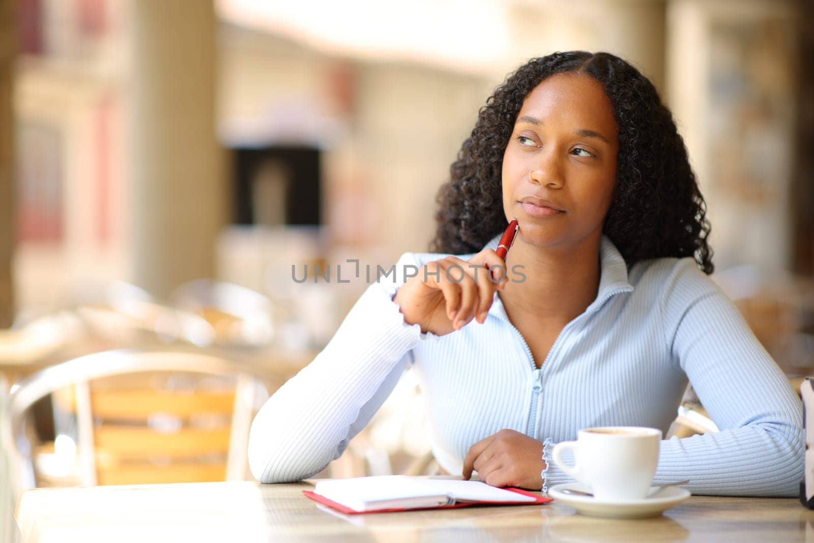 Pensive black woman with an agenda in a bar terrace