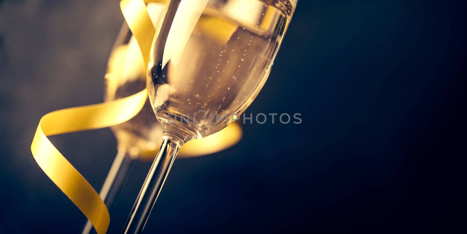 Two champagne glasses with golden ribbon on dark background with copyspace. Luxury restaurant dinner celebration. Classy christmas and new year holiday panoramic design banner.