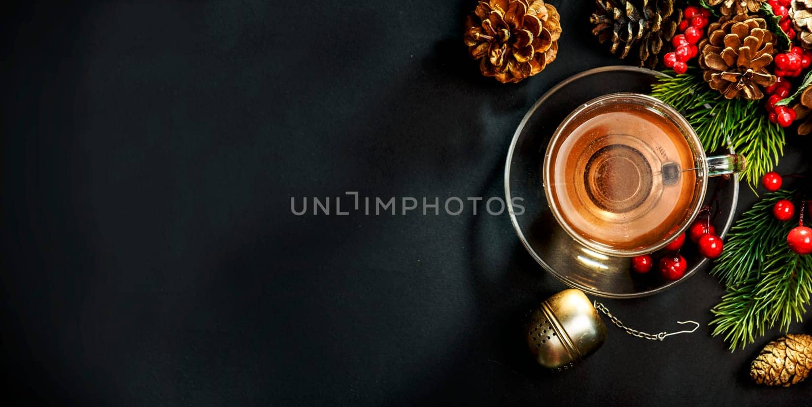 Christmas tea and christmas decoration on black background from above. Cozy winter hot beverage and december pine cones decor on dark table. Top view.