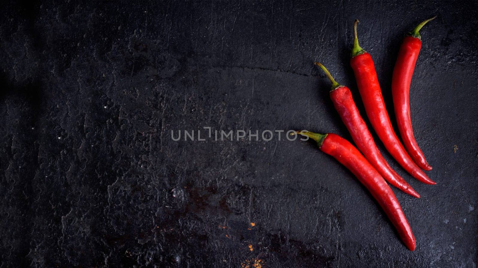 Red hot chili peppers on black rustic textured slate from above. Food background with spicy chilli paprika. Top view.