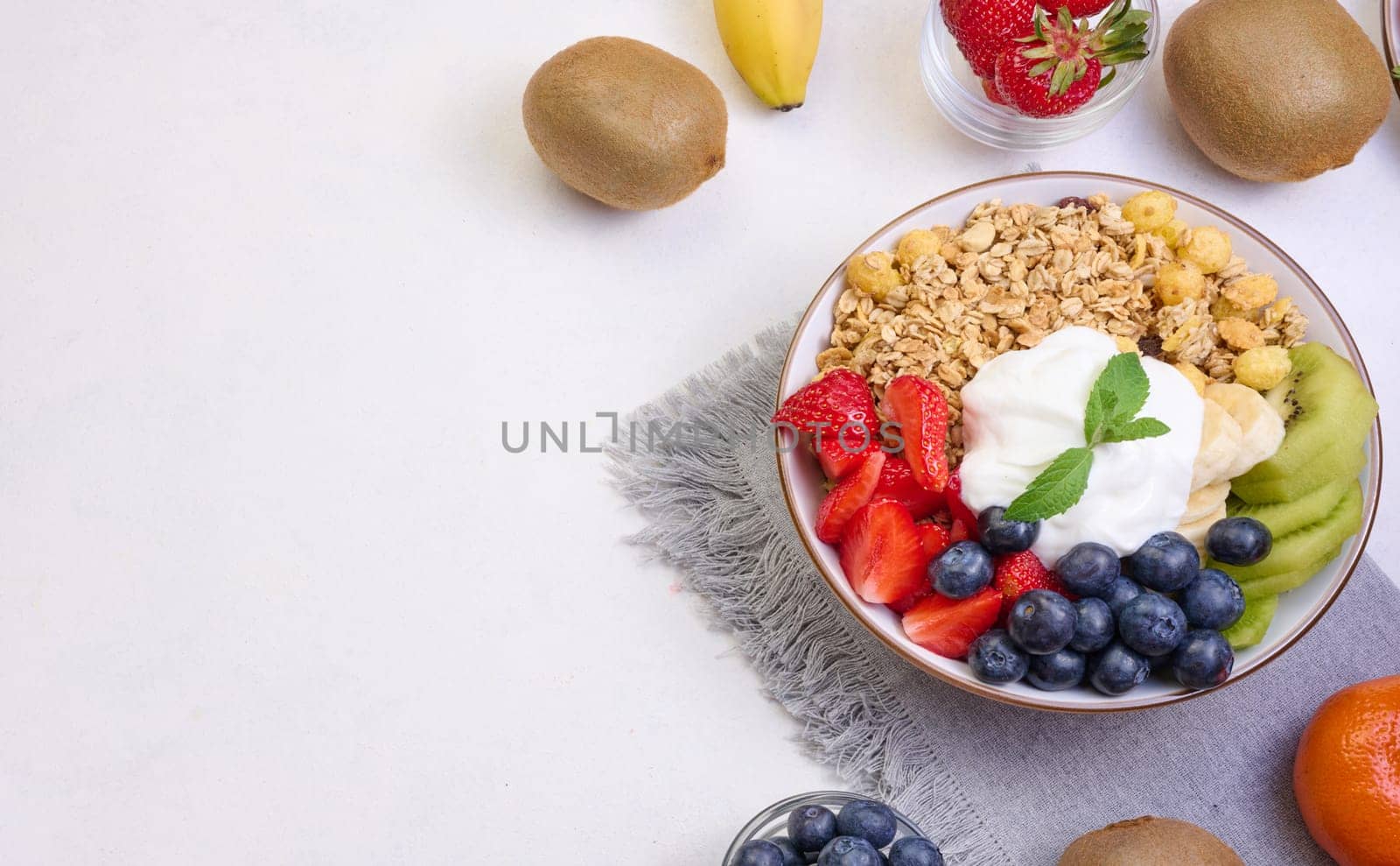 Granola with strawberries, kiwi, banana and blueberries in a round plate on a white table. Healthy and tasty food, top view
