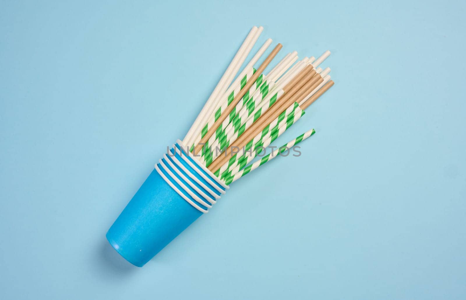 Paper cocktail straws and paper cups on a blue background, top view