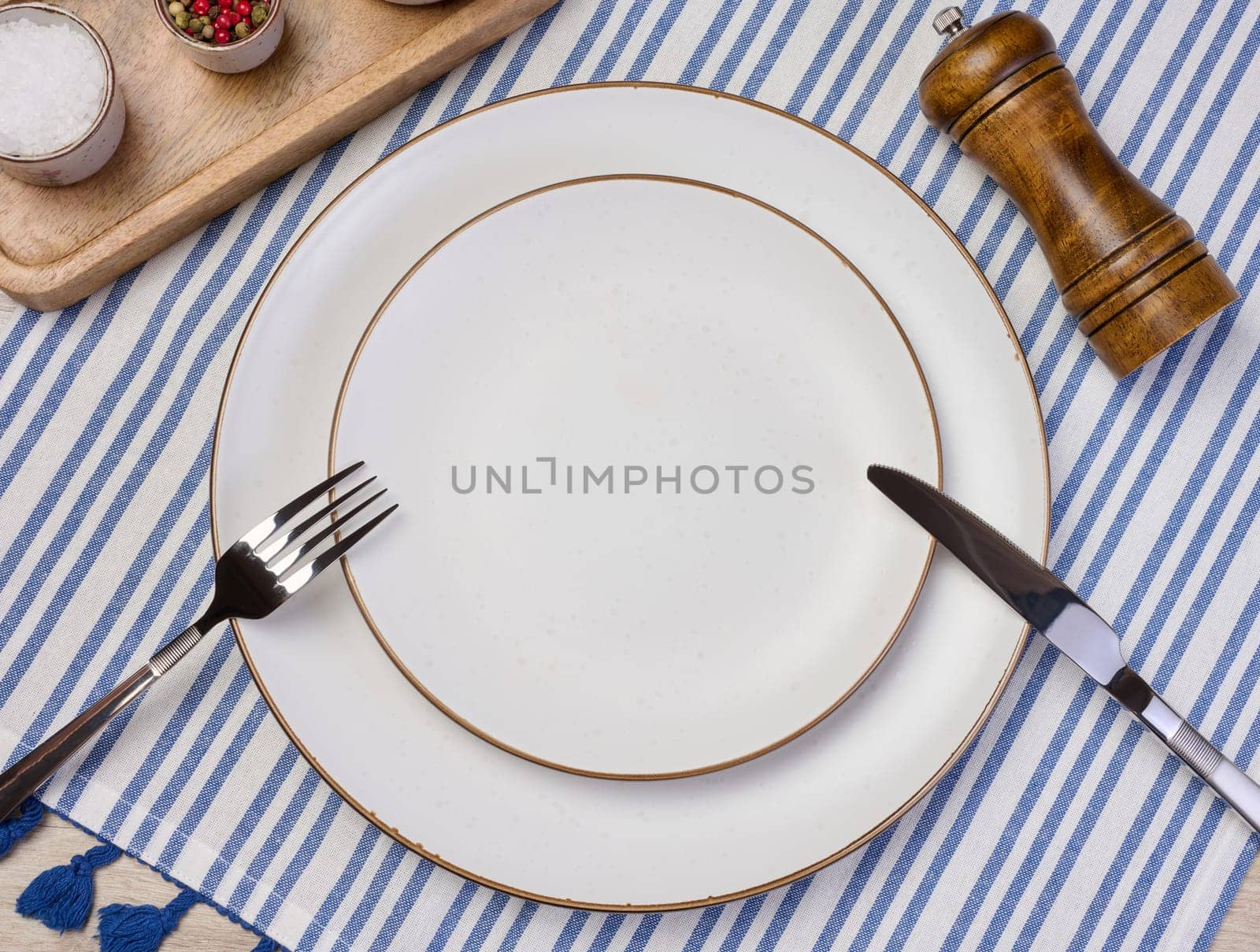 Round empty white ceramic plate, knife and fork on the table, top view