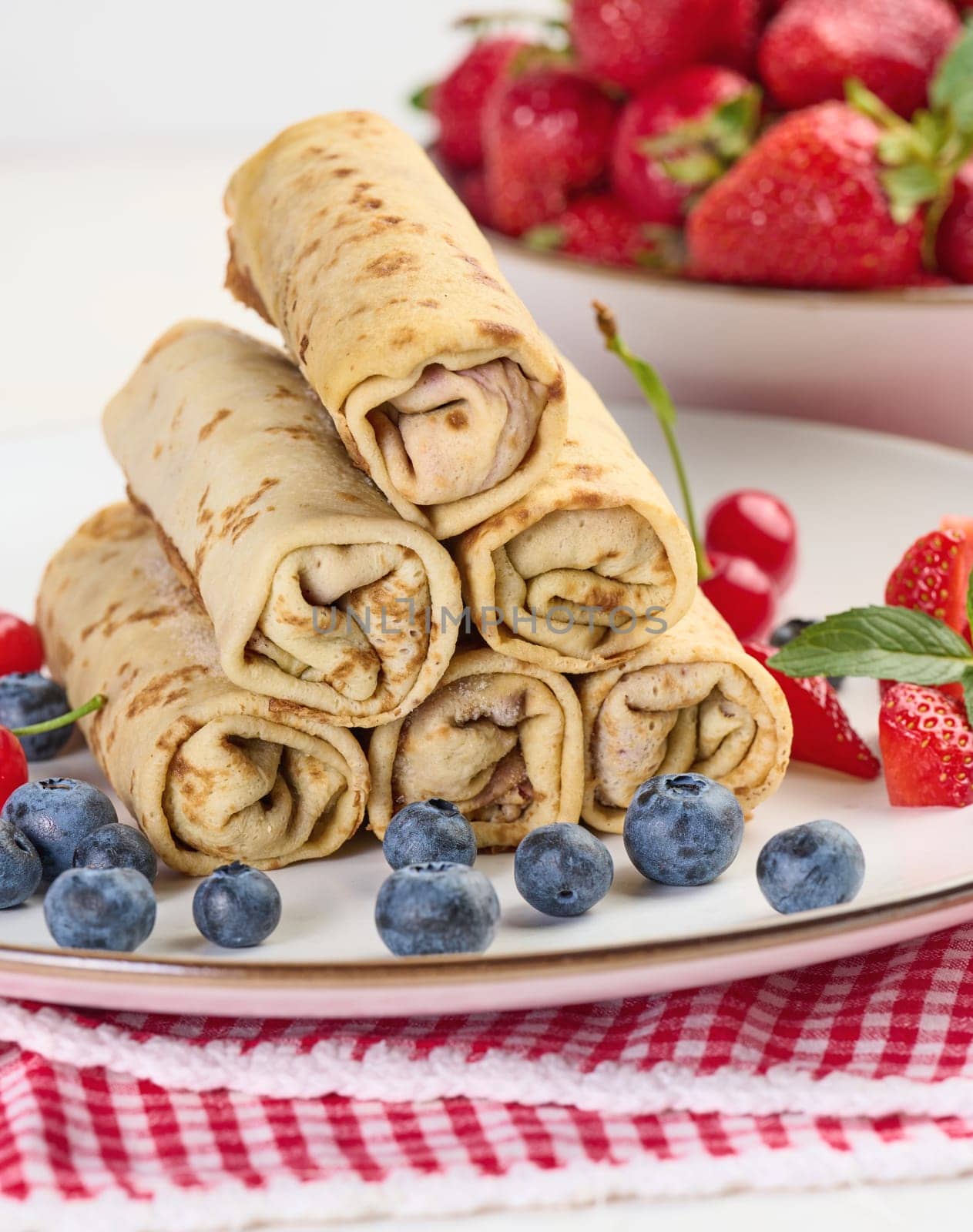 Stack of fried crepes with filling on a round plate, white table