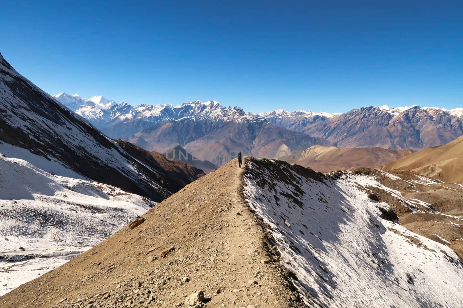 On the way from the Thorong La, Thorung La, Thorang La pass to Muktinath, a person walks on the trail that runs over a small ridge in front of a mountain range, Annapurna Circuit Trek, Nepal 2022