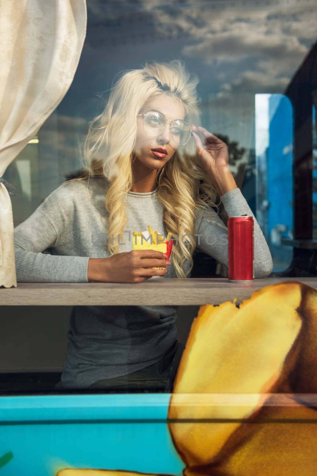 Fast street food concept - beauty young blonde woman eating a burger and soda water into the food truck